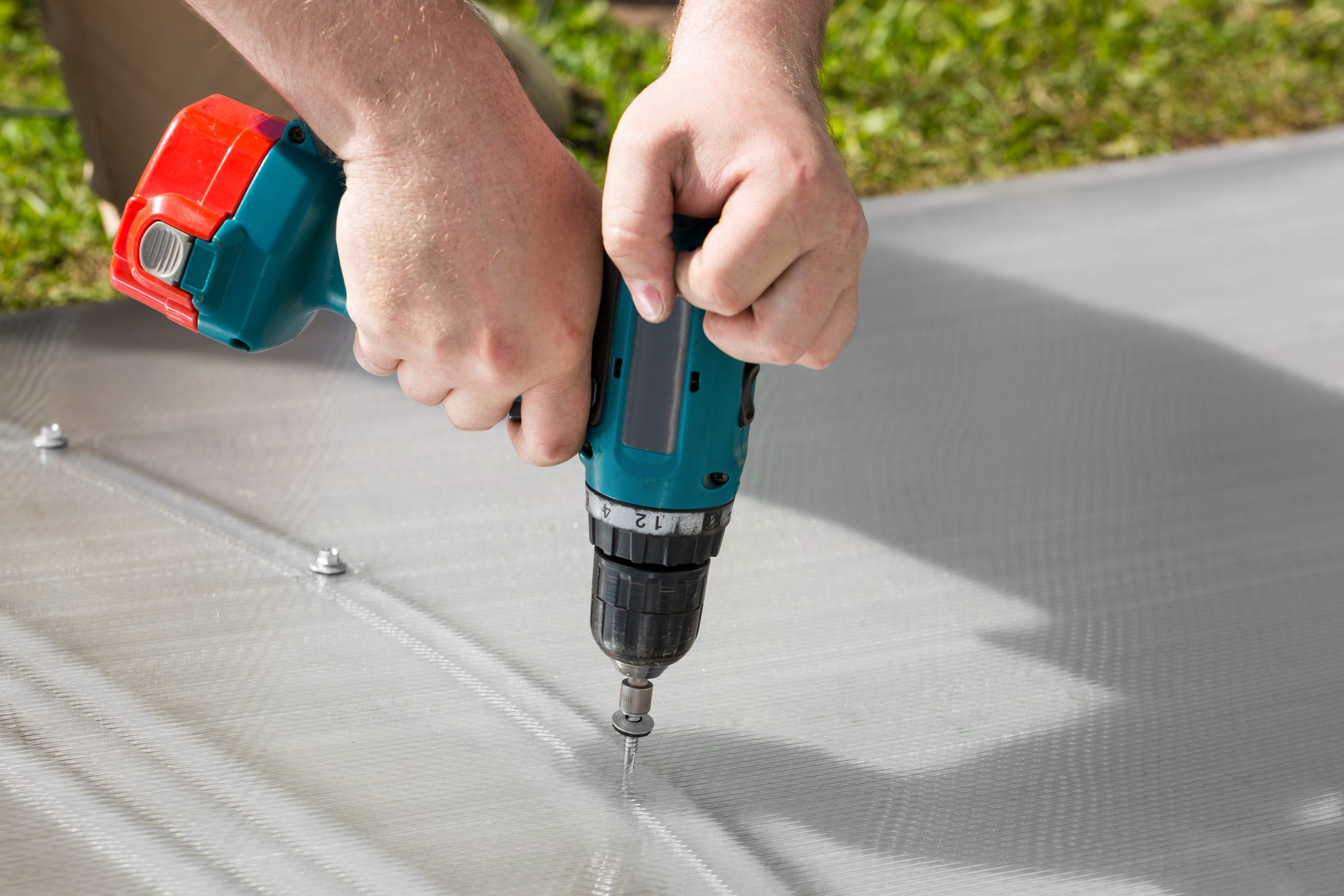 Worker screwing screw into polycarbonate. Building greenhouse